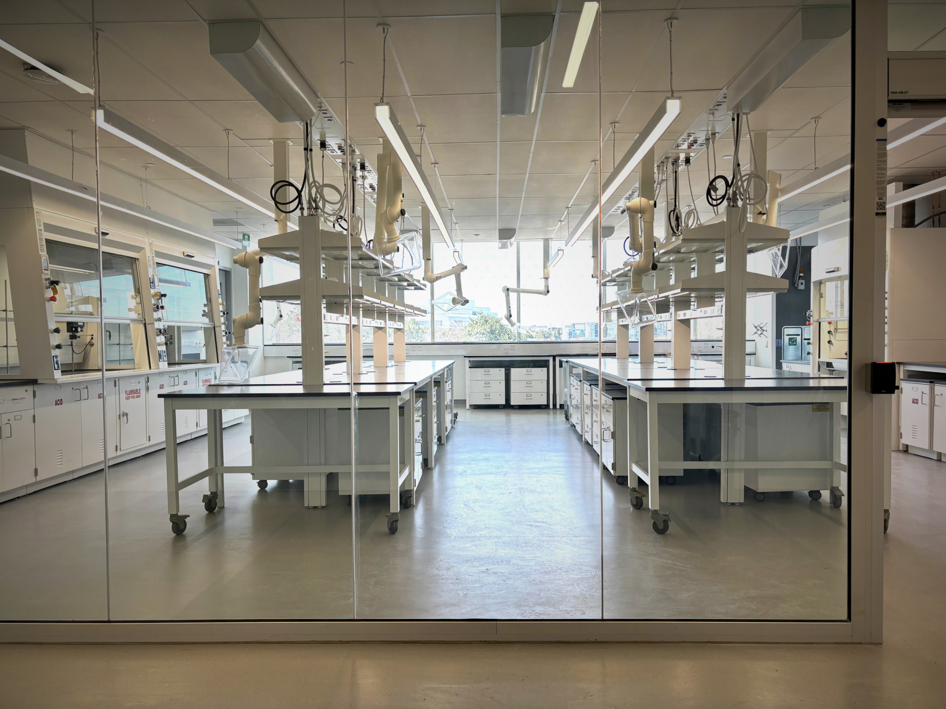 Photo showing the inside of a lab at The National Research Council Canada Advanced Materials Research Facility, featuring fume hoods, benches with shelving, and casework