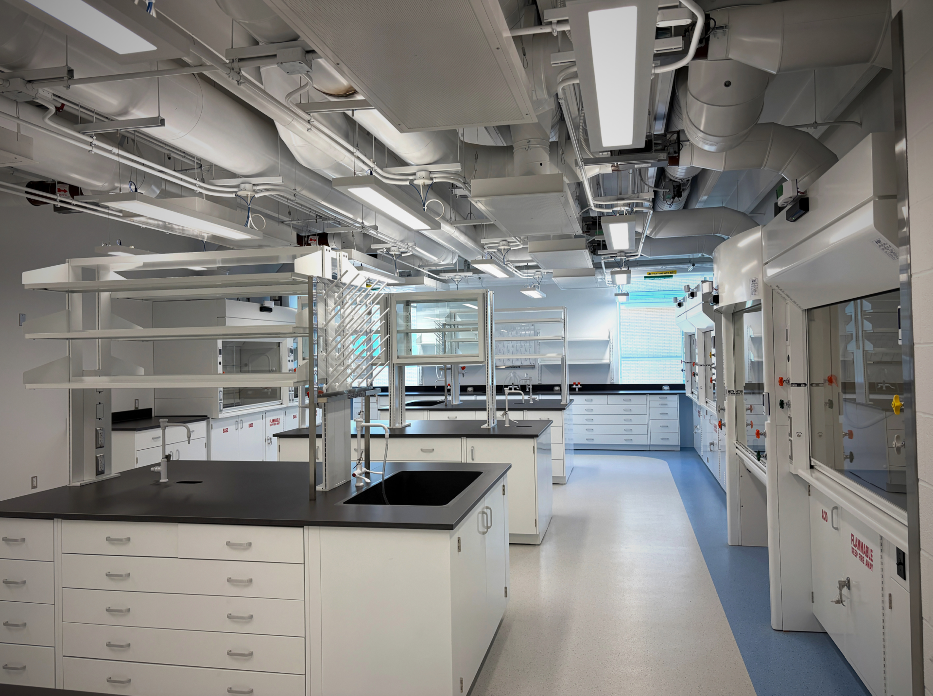 Photo showing the inside of a lab at The University of Waterloo, featuring fume hoods, benchtop shelving, and casework